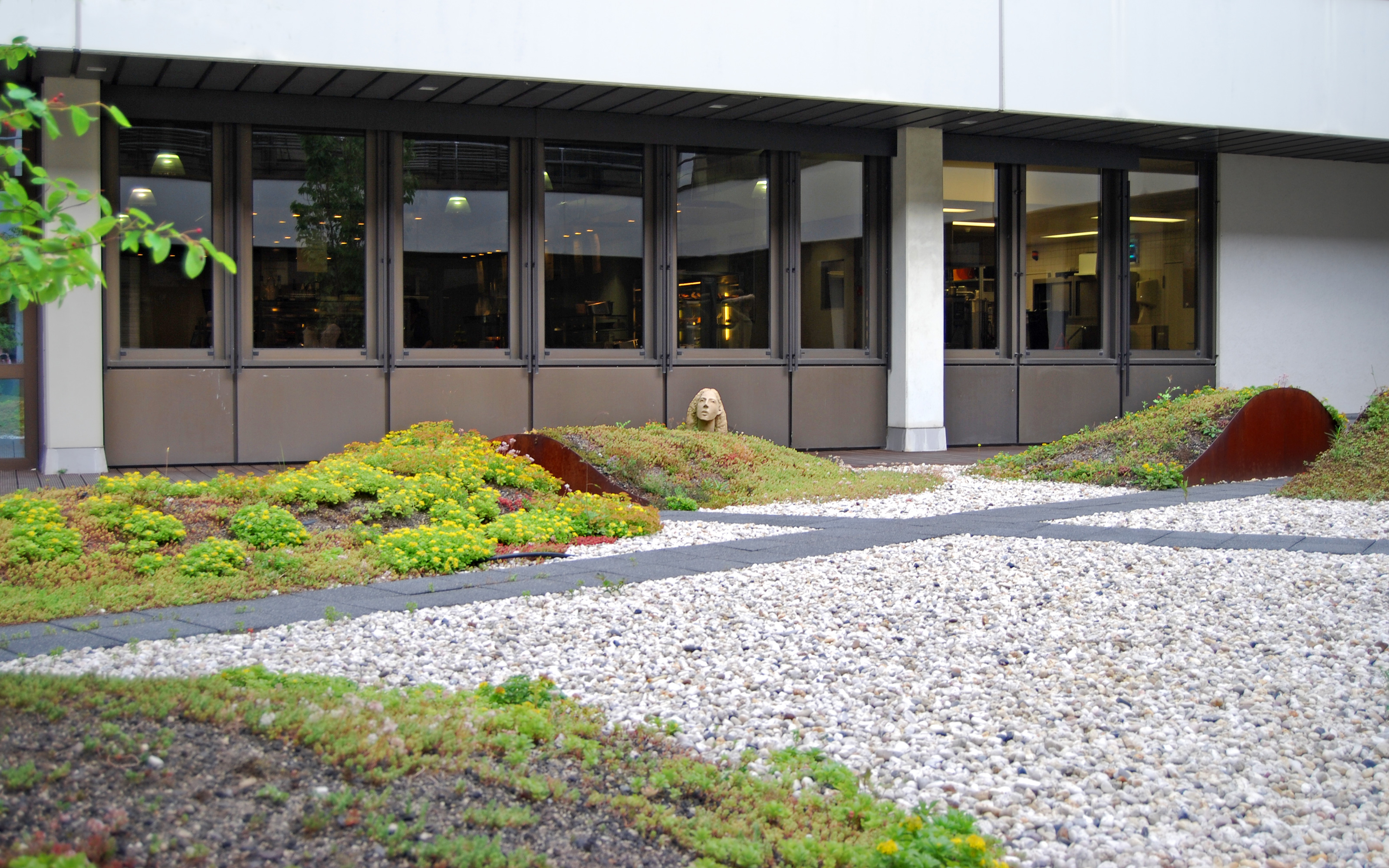 Anhügelung mit Sedum, Kräutern und Skulptur