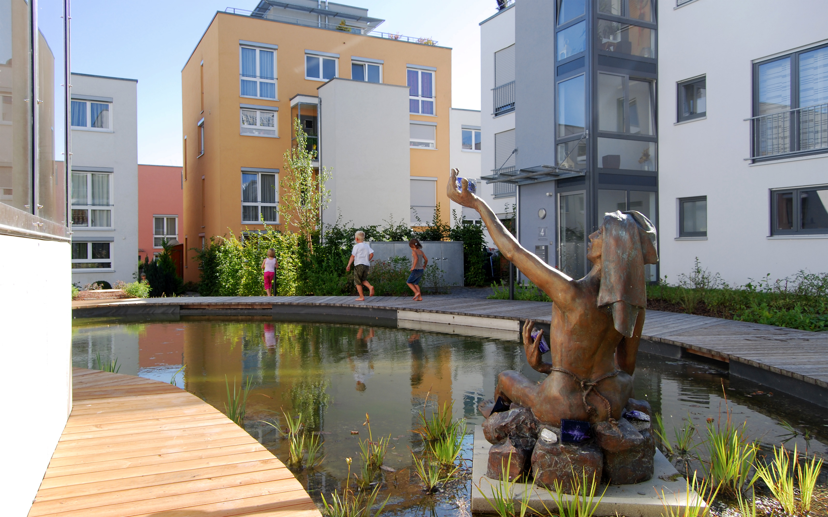 Teich mit Skulptur und Gehbelägen aus Holz in einer Wohnanlage