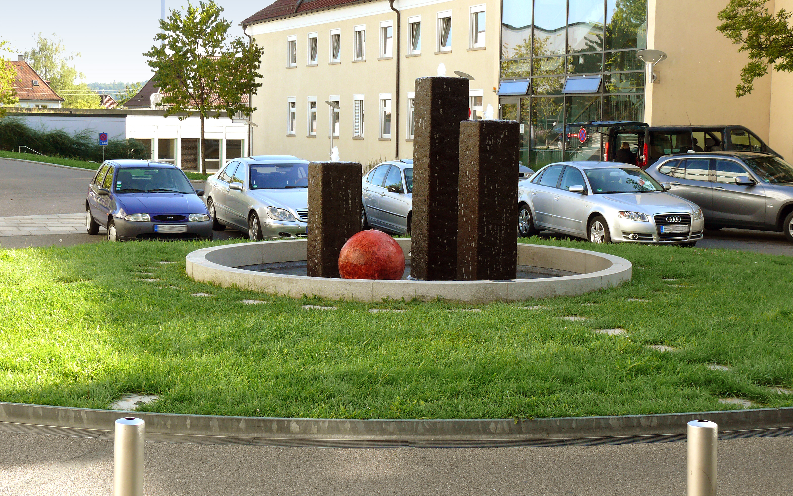 Parkende Autos und Verkehrsinsel mit Wasserspiel und Rasen