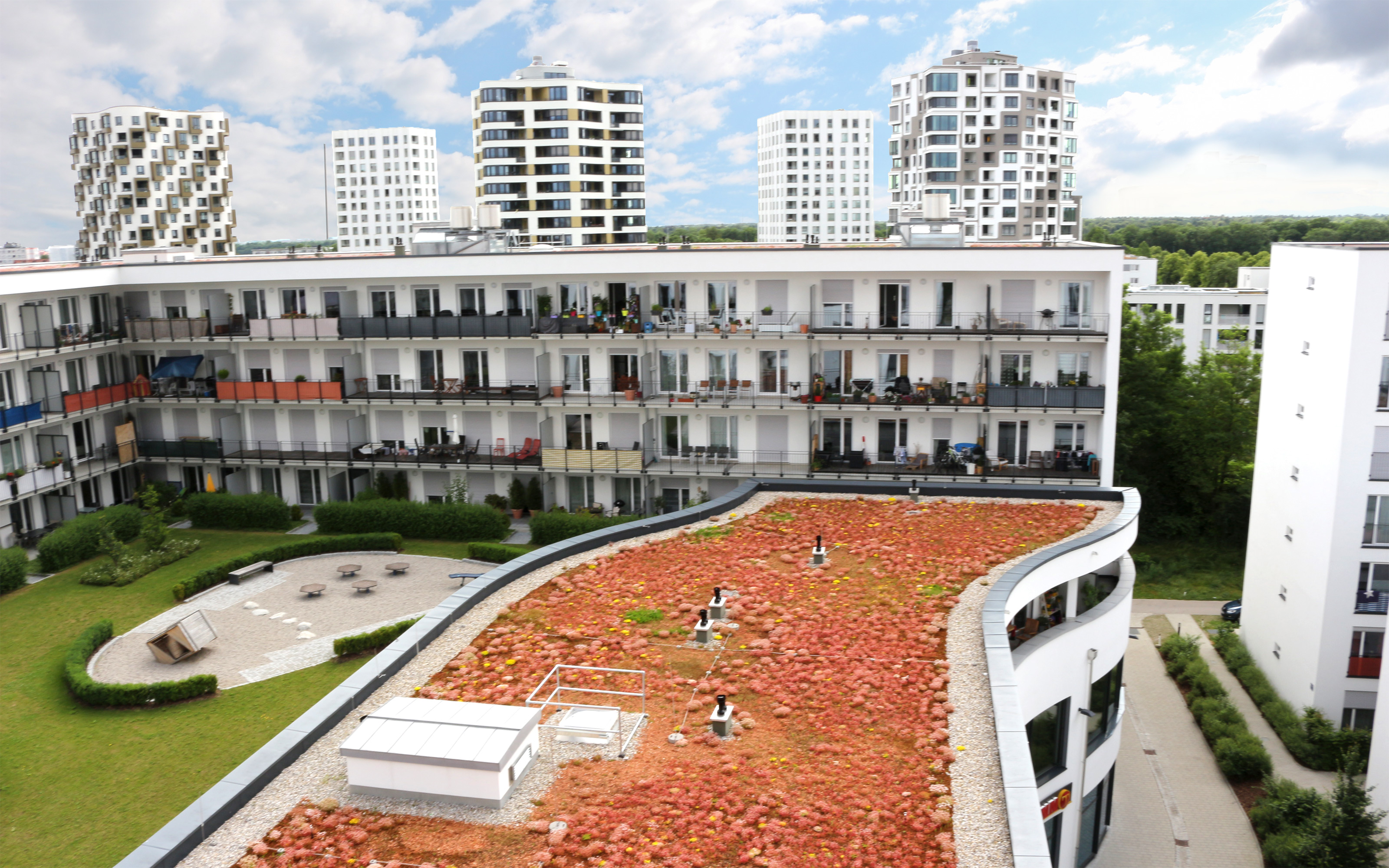 Blick von oben auf ein Sedumdach, Rasenflächen und einen Spielplatz, umgeben von hohen Mehrfamilienhäusern.