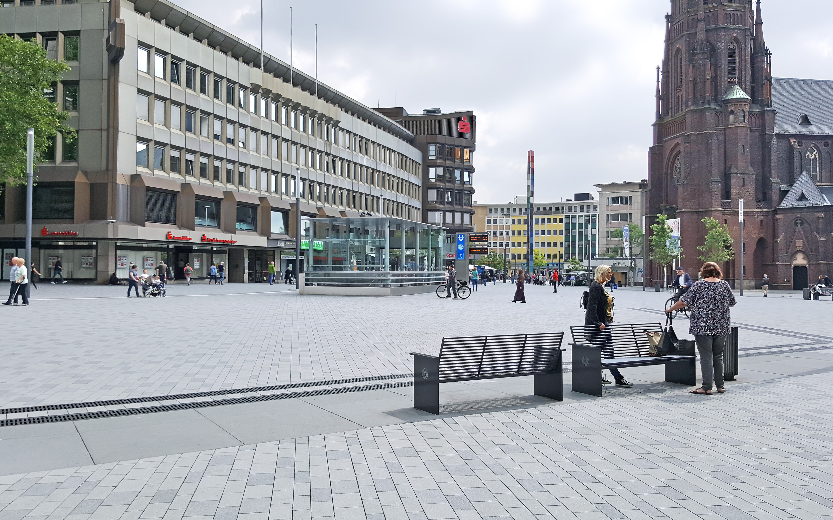 Bänke auf großem Platz, umgeben von Häusern und Kirche