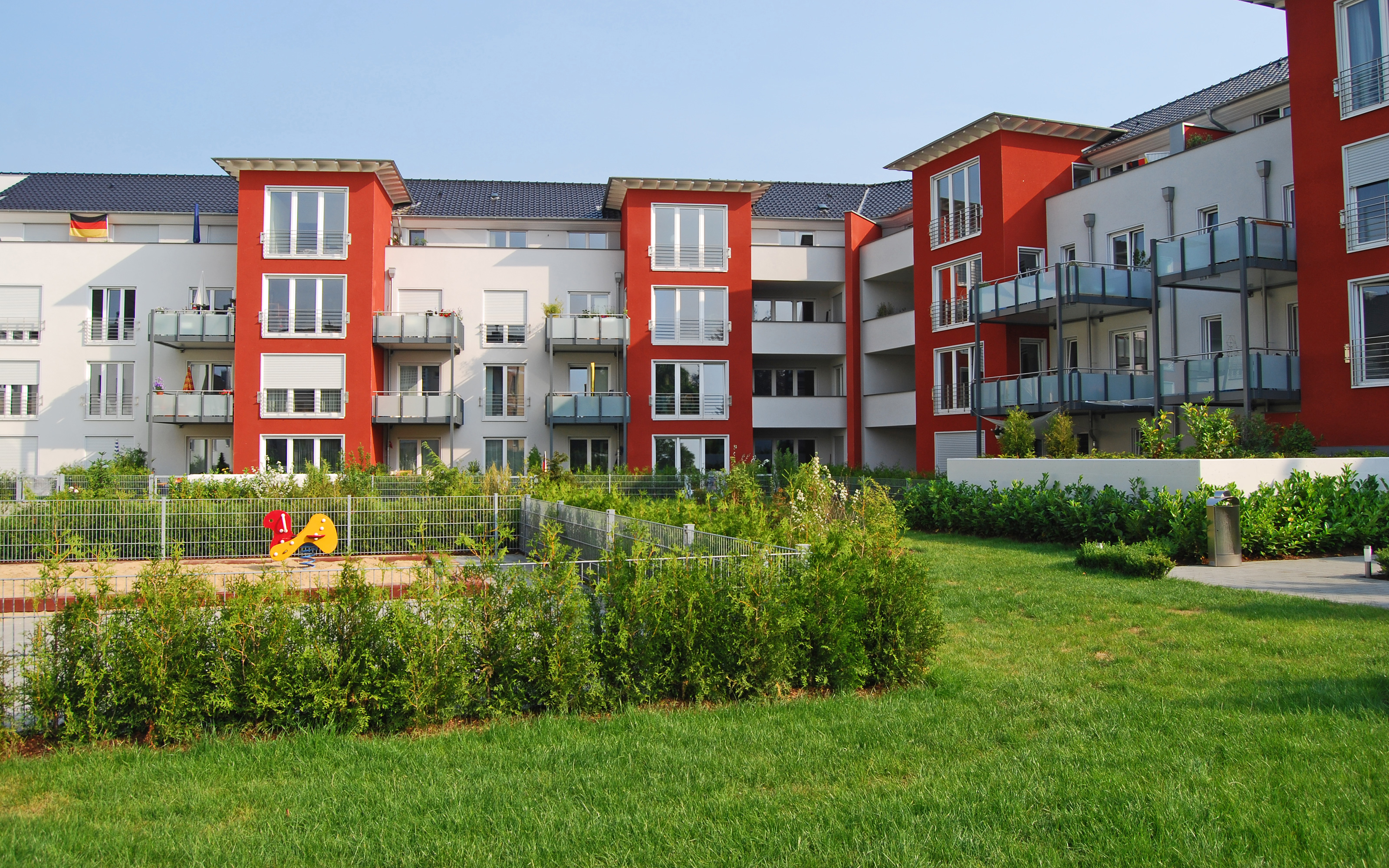 Rasenfläche und mit Büschen umrandeter Spielplatz in einer Wohnanlage