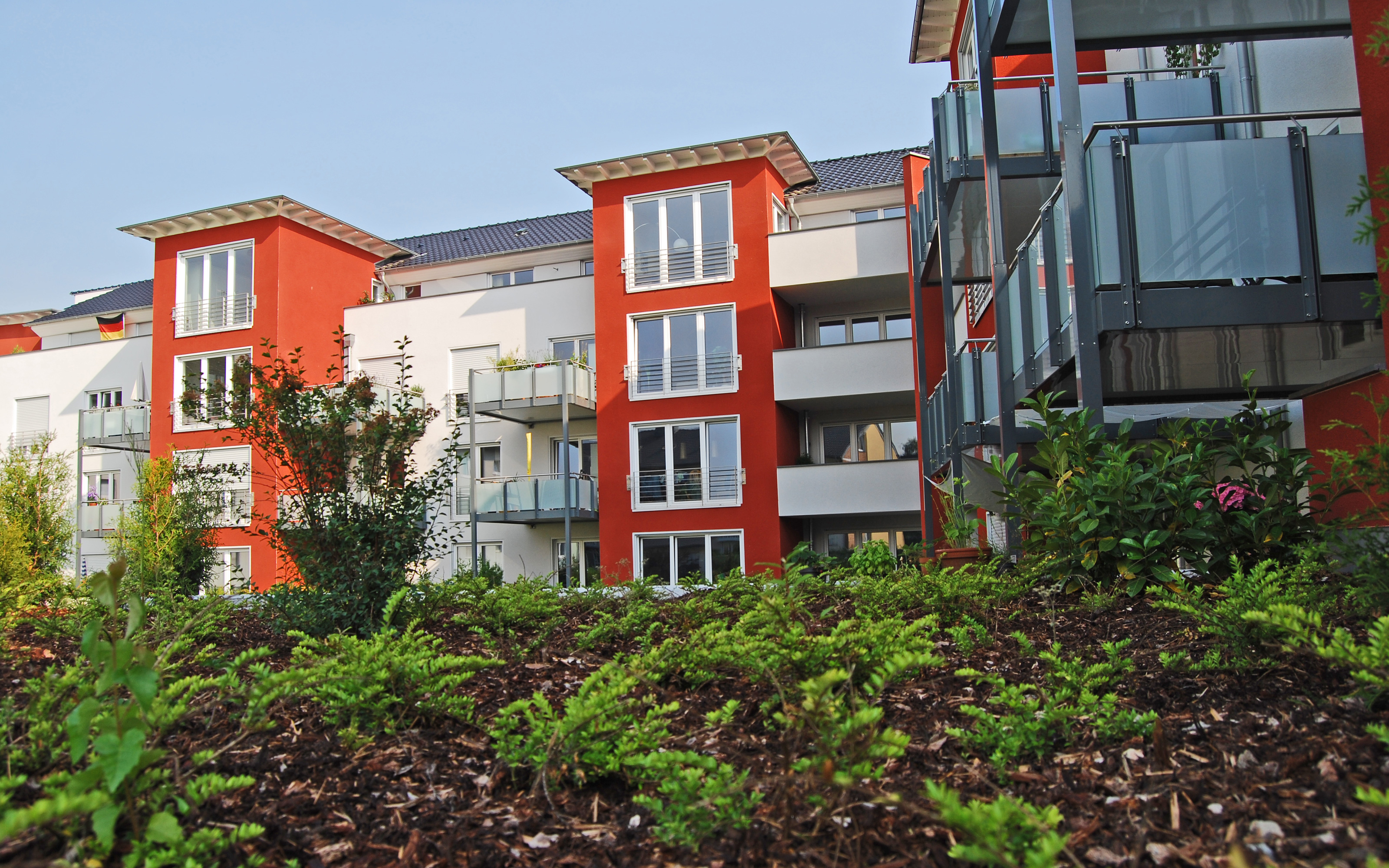 Wohnanlage mit rot-weißen Häusern vor einer Substratanhügelung mit Pflanzen