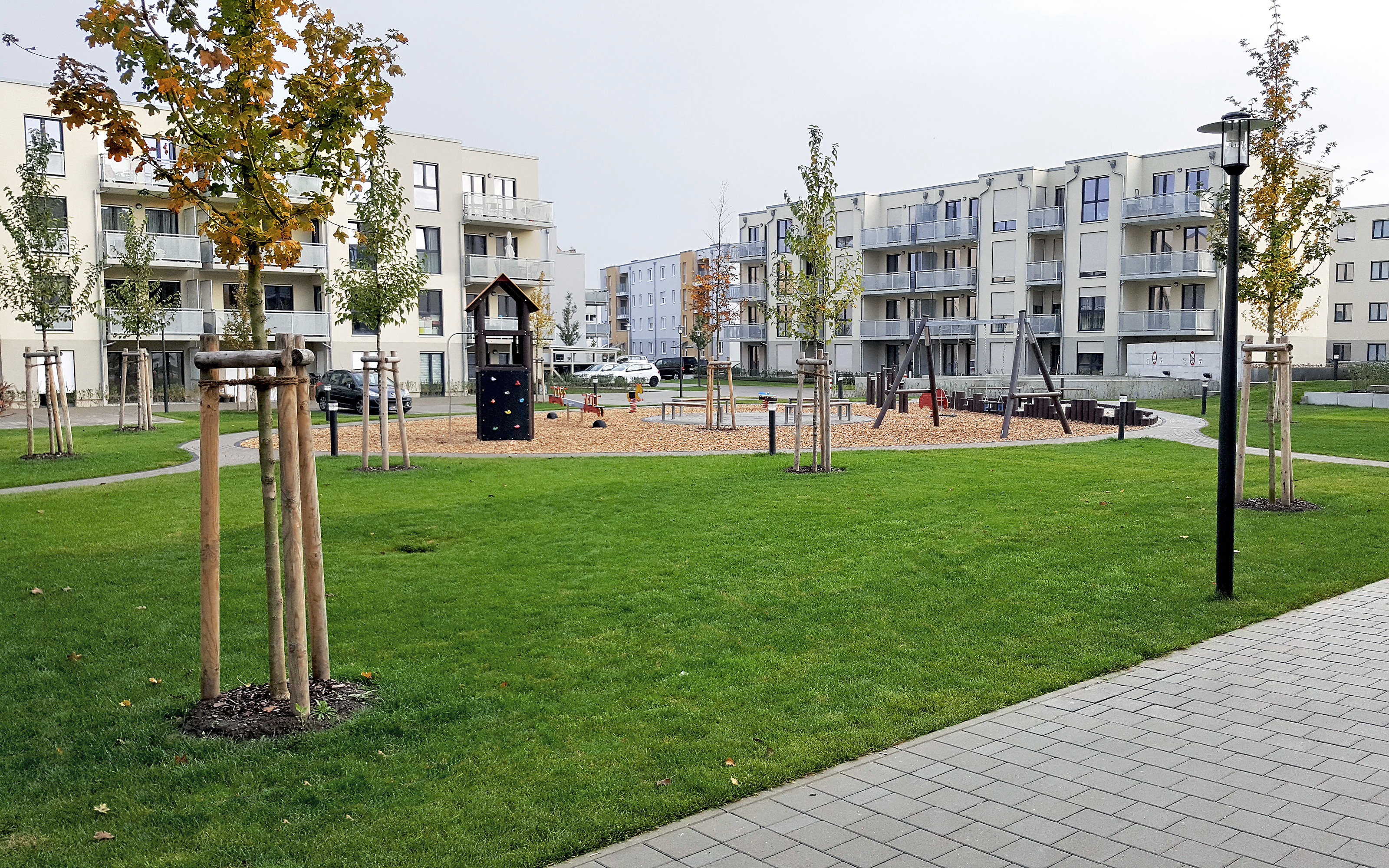 Wohnsiedlung mit Spielplatz, Rasen und kleinen Bäumen