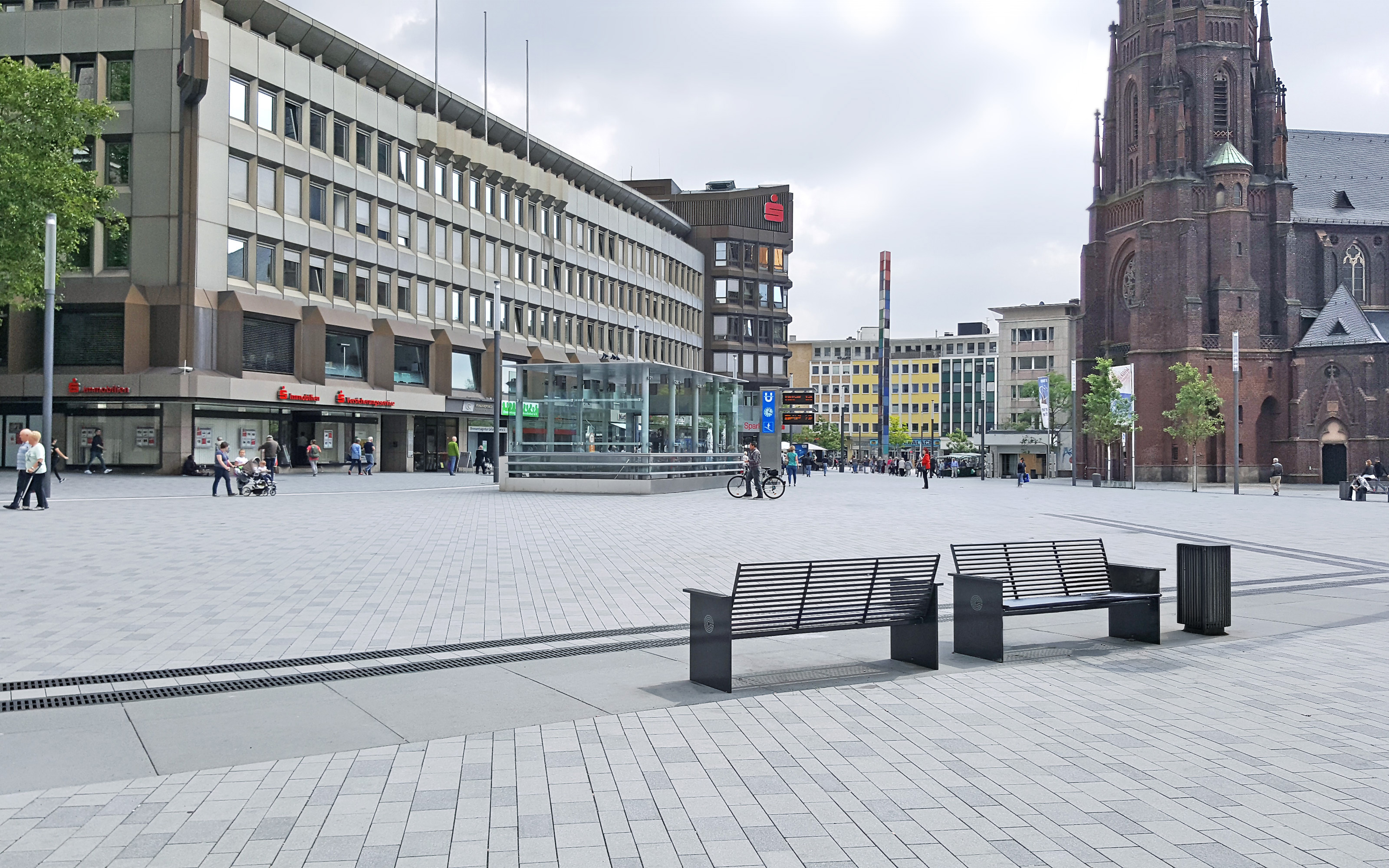 Bänke auf großem Platz, umgeben von Häusern und Kirche