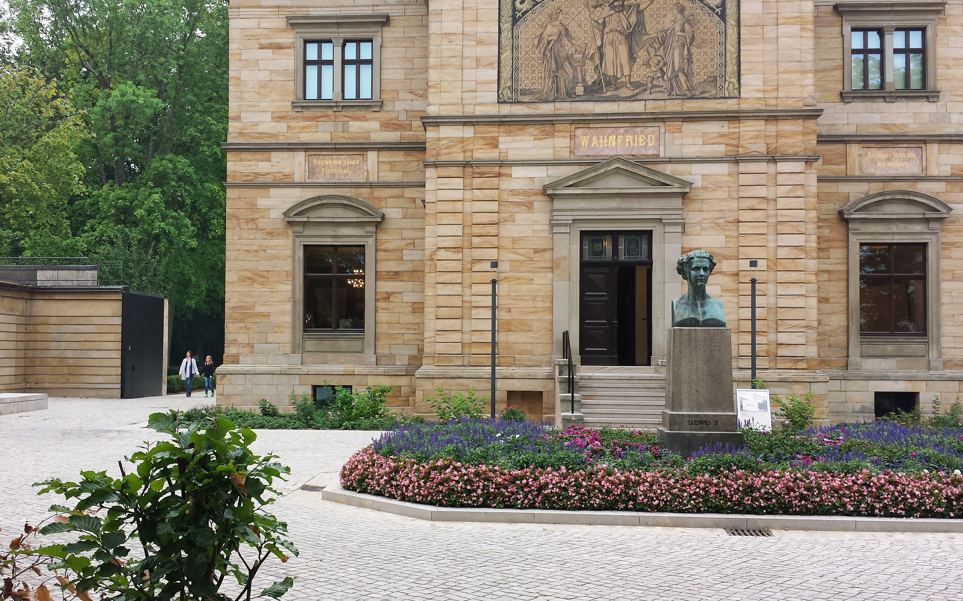 Blumenbeet und Stein-Skulptur vor einem historischen Gebäude