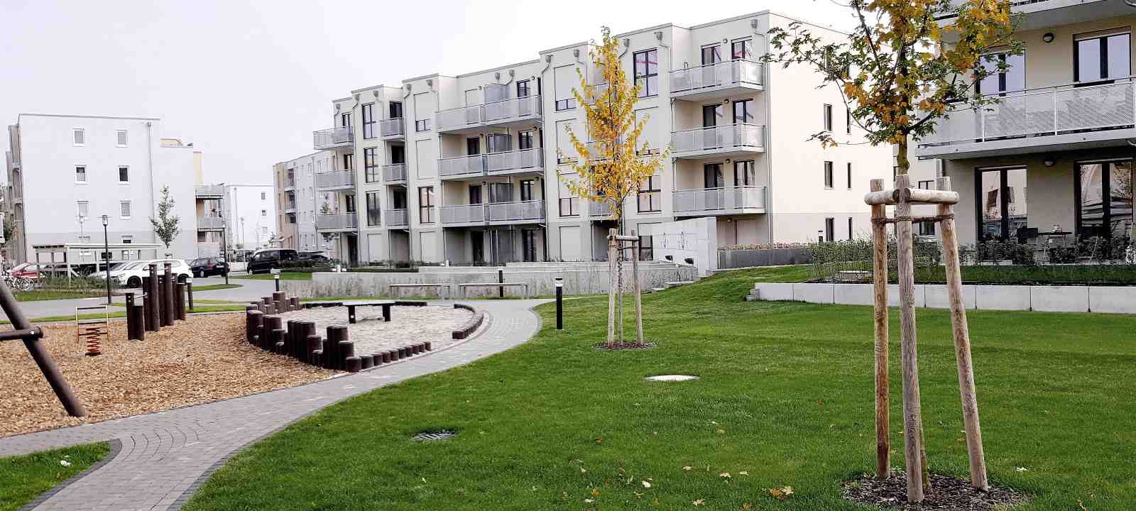 Wohnsiedlung mit Spielplatz, Rasen, kleinen Bäumen und Parkplätzen