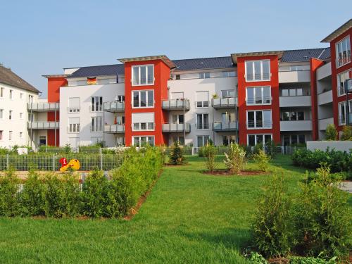 Wohnanlage mit rot-weißen Häusern, gruppiert um eine Rasenfläche mit Sträuchern und Spielplatz