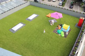 Eine schöne Rasenfläche zum Entspannen, Spielen und Genießen entstand auf dem Dach dieser Lagerhalle, an welche das neue Wohngebäude angrenzt. Rasenfläche mit Spielbereich für Kinder auf dem Dach