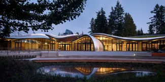 Das geschwungene Dach scheint gleichsam zu schweben über dem beleuchteten Raum. © Nic Lehoux, Courtesy: Perkins + Will Gebäude mit geschwungener Dachform bei Nacht