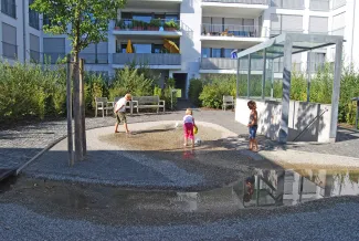 Spielende Kinder an Springbrunnen und vor dem Treppenaufgang von der Tiefgarage