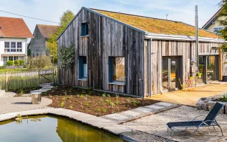 Teich vor einem begrünten Holzhaus