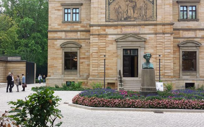 Blumenbeet und Stein-Skulptur vor einem historischen Gebäude