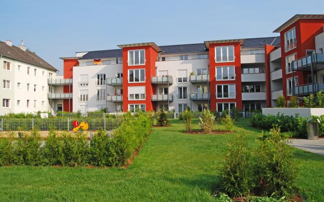 Wohnanlage mit rot-weißen Häusern, gruppiert um eine Rasenfläche mit Sträuchern und Spielplatz